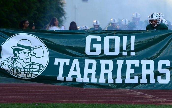 Football players run through banner with the words GO!! Tarriers